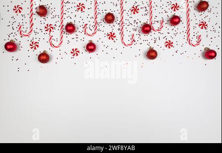 Christmas composition, red and white sweets, candy canes, round candies, red baubles, stars confetti on white background. Stock Photo