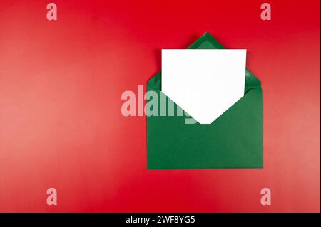Top view of green envelope, white card on red background. Christmas, New Year composition. Post flat lay, copy space. Stock Photo