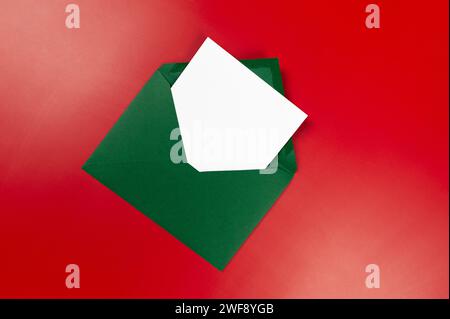 Top view of green envelope, white card on red background. Christmas, New Year composition. Post flat lay, copy space. Stock Photo