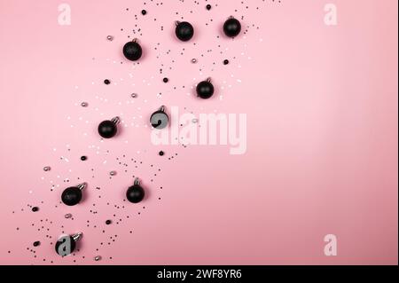 Christmas composition, black decorations, black baubles, silver stars confetti on pink background. Christmas, new year, winter concept. Stock Photo