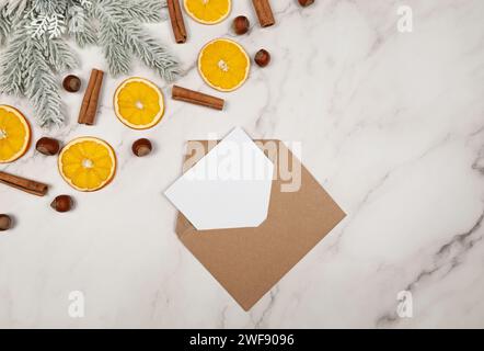 Christmas composition, dried orange slices, fir tree branches, cinnamon sticks, hazelnuts on white marble background. Kraft envelope. Stock Photo