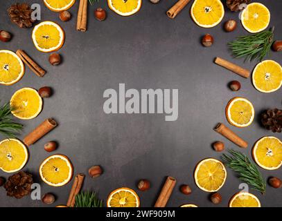 Christmas composition, dried orange slices, fir tree branches, cinnamon sticks, pine cones, hazelnuts on black stone background. Stock Photo