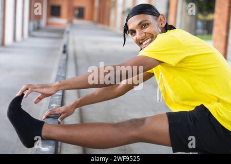 Joyful urban dancer stretching his leg on a handrail, preparing for a dance routine outdoors. Stock Photo