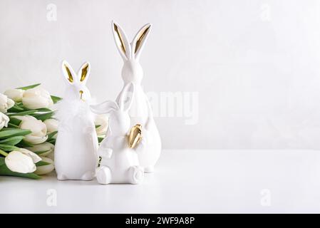 Three Easter rabbits figurines with bouquet of white tulips on white background. Easter celebration concept. Copy space. Front view Stock Photo