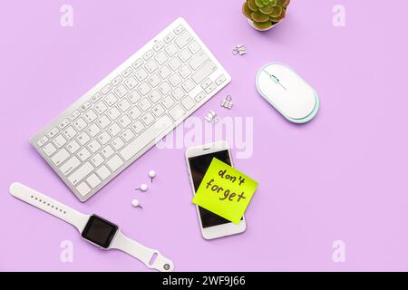 Sticky note with text DON'T FORGET, gadgets and paperclips on lilac background Stock Photo