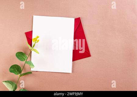 Red envelope with empty white card for text and eucalyptus branches on beige background. Blank invitation or greeting card mockup with copy space Stock Photo