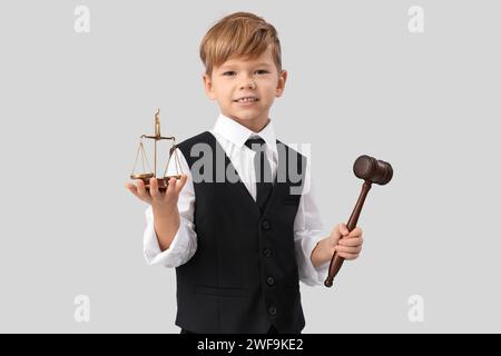 Cute little judge with gavel and justice scales on light background. Opposite Day celebration Stock Photo