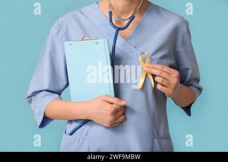 Doctor holding golden ribbon and clipboard on blue background. Childhood cancer awareness concept Stock Photo