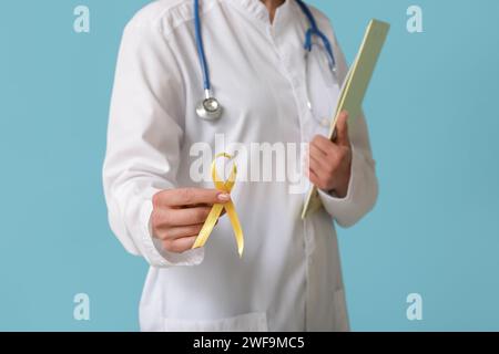 Doctor holding golden ribbon and clipboard on blue background. Childhood cancer awareness concept Stock Photo