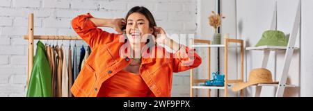 delighted asian fashion designer posing in bright orange clothes in studio, horizontal banner Stock Photo