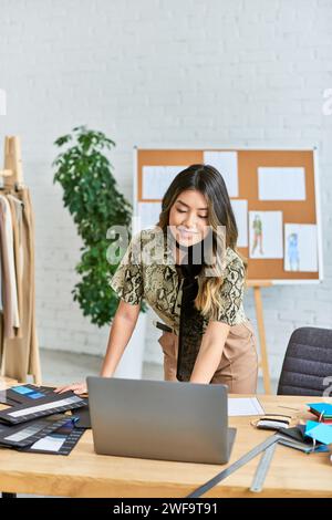 happy asian personal stylist working near laptop and color samples in own fashion atelier, business Stock Photo
