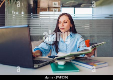 Young businesswoman working online in office using laptop. Middle-aged woman teacher searching for information sitting at desk. Stock Photo