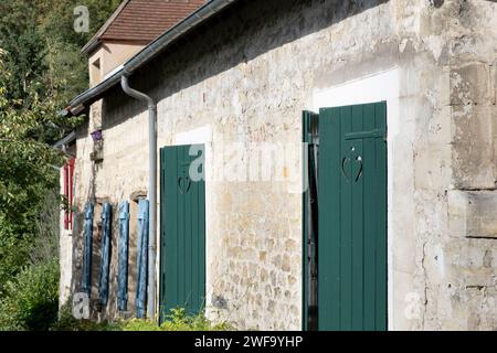 House in Auvers-sur Oise in France with weathered plastered walls and windows with different colored shutters, red, blue and green Stock Photo