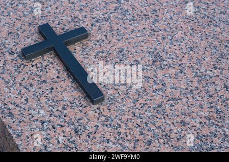 Simple black metal cross on a mixed marbled gravestone Stock Photo