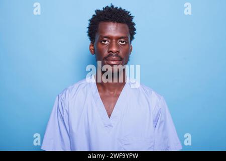 Close-up of black nurse posing alone in front of blue background with copy space for advertising. Photograph showing an African American man in blue scrubs facing the camera in profile. Stock Photo