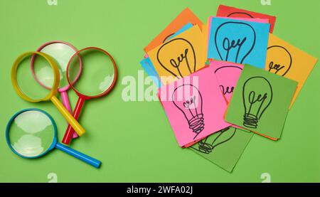 Drawn light bulbs on sheets of paper and a plastic magnifying glass, the concept of searching for new ideas. Stock Photo