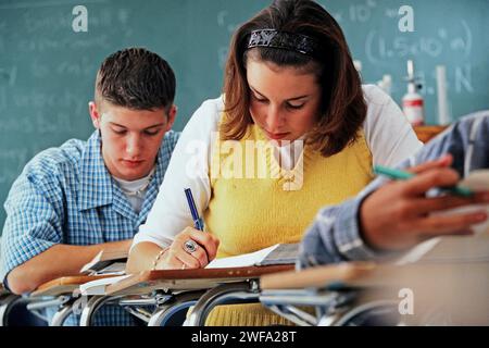 A female Caucasian High school student writing in her notebook in her notebook while busily working at her desk in class Stock Photo