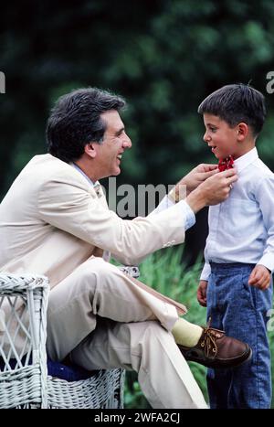 A father dressed in a white suit helps his young son dress with a bowtie Stock Photo
