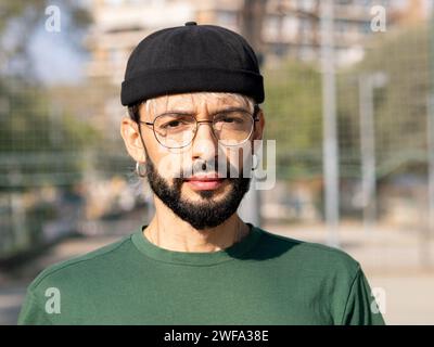 Portrait of a young millennial man with glasses and hat looking at camera in a city Stock Photo