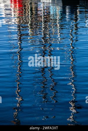 The serene blue water creates a mesmerizing abstract pattern as it reflects the distorted silhouette and lights of boats at dusk. Stock Photo