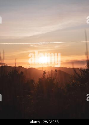 Golden hour with the sun setting behind the rolling hills and wind turbines. Taken at Makara, New Zealand Stock Photo