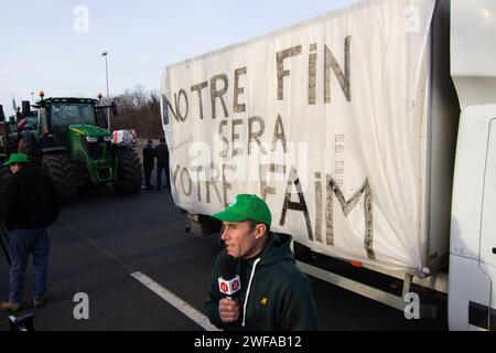 Argenteuil, France. 29th Jan, 2024. A farmer talks to the press in front of a truck that has tagged 'Our end will be your hunger', during the block of the A15 highway, in the outskirts of Paris. Following the French farmers' strike, the beginning of the week was marked by the blocking of eight of the main access points to the French capital. In Argenteuil, north of Paris, around 30 tractors blocked the A15 highway. Credit: SOPA Images Limited/Alamy Live News Stock Photo