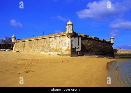 Golden sand on the beach at Lagos, with the old harbour defenses, the 17th century Forte Bandeira, under a deep blue sky, Algarve, Portugal Stock Photo