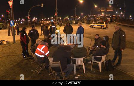 Hamburg, Germany. 30th Jan, 2024. Protesters sit around a fire barrel at the edge of a blockade at an intersection with access to the port in the south of Hamburg. The farmers' protests continued into Tuesday night. The farmers continue to paralyze the main traffic arteries around the port of Hamburg. The action has far-reaching consequences for the suppliers and leads to considerable traffic obstructions. Credit: Steven Hutchings/dpa/Alamy Live News Stock Photo