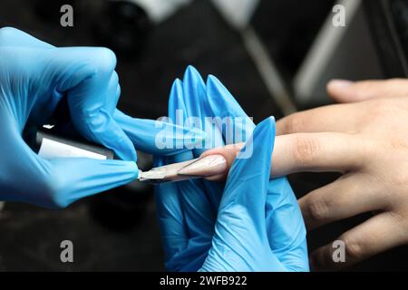 Close-up of professional nail sculpting, highlighting a nail technician's precision in creating a sleek stiletto shape using specialized tools in a be Stock Photo