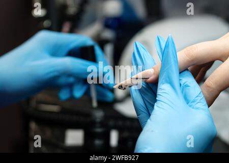 Close-up of professional nail sculpting, highlighting a nail technician's precision in creating a sleek stiletto shape using specialized tools in a be Stock Photo