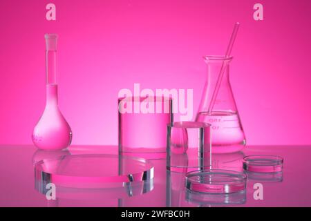 Transparent podium in round and cylinder shape are decorated on pink background with laboratory glassware containing fluid. Stage showcase on pedestal Stock Photo