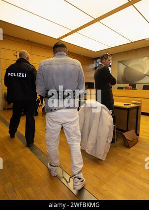 30 January 2024, Bavaria, Würzburg: The defendant (M) is brought to the courtroom at Würzburg Regional Court in handcuffs and shackles. More than ten months after the fatal stabbing of a woman in Lower Franconia, the district court is hearing the case against her husband. The public prosecutor is accusing the 36-year-old of murder. Photo: Heiko Becker/dpa Stock Photo