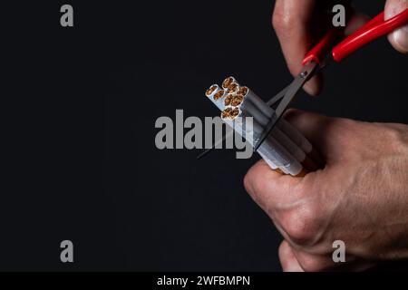 Quit smoking. Closeup of man hands holding bunch of cigarettes and cutting them in halves with scissors. Stop Smoking Cigarette Concept. Stock Photo