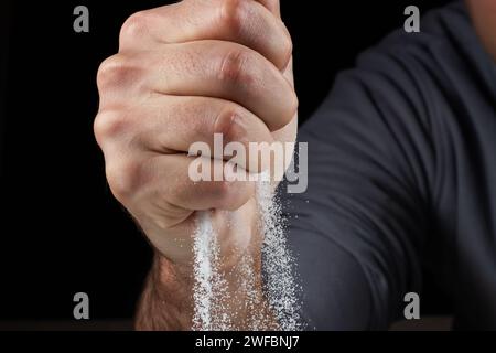 Man with handful of white dry sand in her hands, spilling sand through fingers on black background. Concept of flow of life. Close up of grains of pur Stock Photo