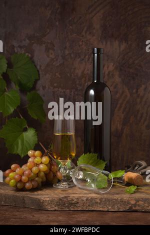 The concept of a delicious alcoholic drink, wine and grapes. Wine bottle, cork, corkscrew, empty glass and glass of white wine and bunch of pink grape Stock Photo