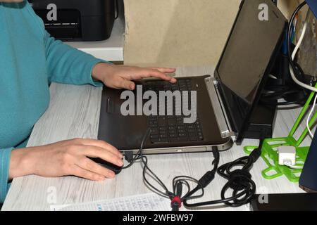 A woman in a blue blouse sits at a table. Her hand lies on the computer mouse. She beeps with the finger of her other hand. Stock Photo