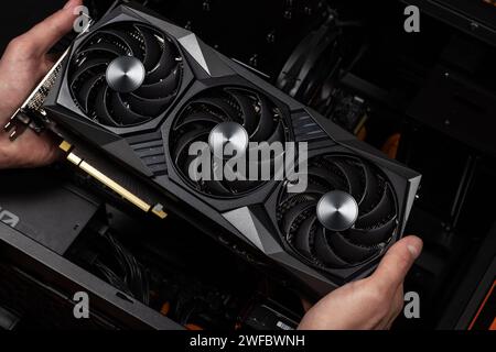 Installing video card in an open case of personal computer. Graphics adapter or graphics card in the hand of a technician. PC assembly and upgrade. Stock Photo
