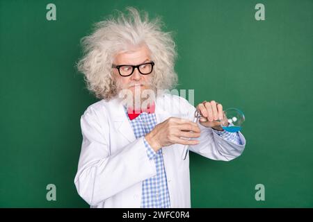 Photo of funky funny serious mad scientist with messy hair doing crazy experiment isolated on green color background Stock Photo