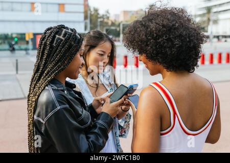 Women and transgender friend using phone in the street Stock Photo