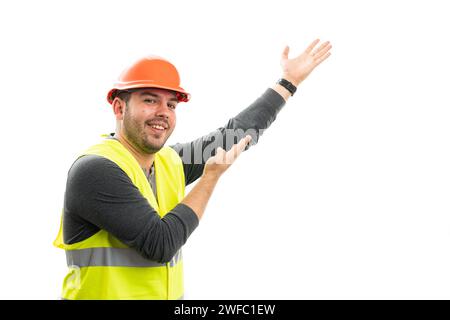 Cheerful builder man with friendly expression wearing work attire helmet and vest presenting blank copyspace for advertising with palms isolated on wh Stock Photo