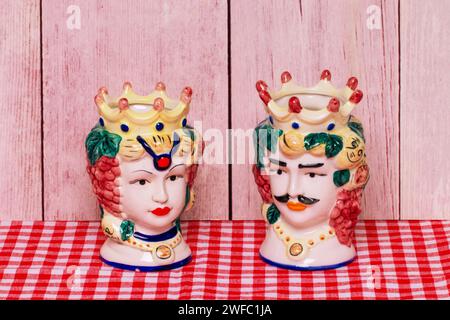 Souvenir from Sicily. Traditional sicilian ceramic pots or vases with heads of a couple of lovers of Moorish heads on red checked napkin of wooden wal Stock Photo