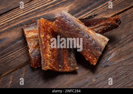Pieces of cleaned dried fish on wooden background. Dry Peppered Pollack. Amber with pepper. Stock Photo