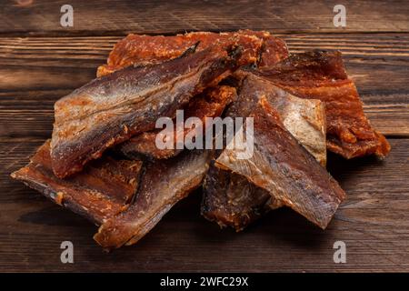 Pieces of cleaned dried fish on wooden background. Dry Peppered Pollack. Amber with pepper. Stock Photo