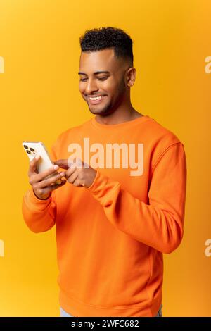 Happy Indian man in casual clothes using smartphone isolated on yellow, guy chatting online, using new mobile app, texting with girlfriend Stock Photo