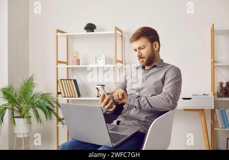 Young business man using mobile phone and laptop computer while sitting on chair at home Stock Photo