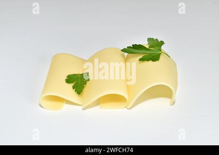 Several thin pieces of cheese with green leaves lie on white. Stock Photo