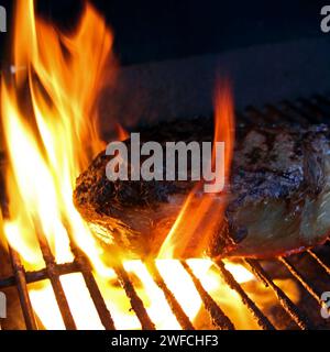 Rib eye on a grill, surrounded by flames. Searing the steak before cooking at a reduced temperature. Extra thick cut of ribeye steak on a grill top. Stock Photo