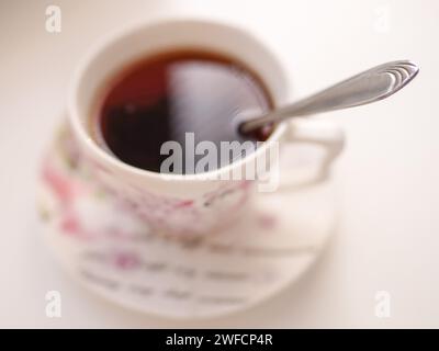 Spoon in a cup of drink. Cup of tea on a saucer in blur on a white table Stock Photo