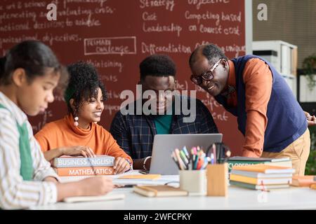 Smiling Black teacher helping students working on group project together and using laptop Stock Photo