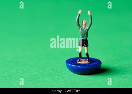 A single Subbuteo miniature goalkeeper figure painted in a green shirt  and black shorts. Subbuteo is a popular tabletop football game Stock Photo